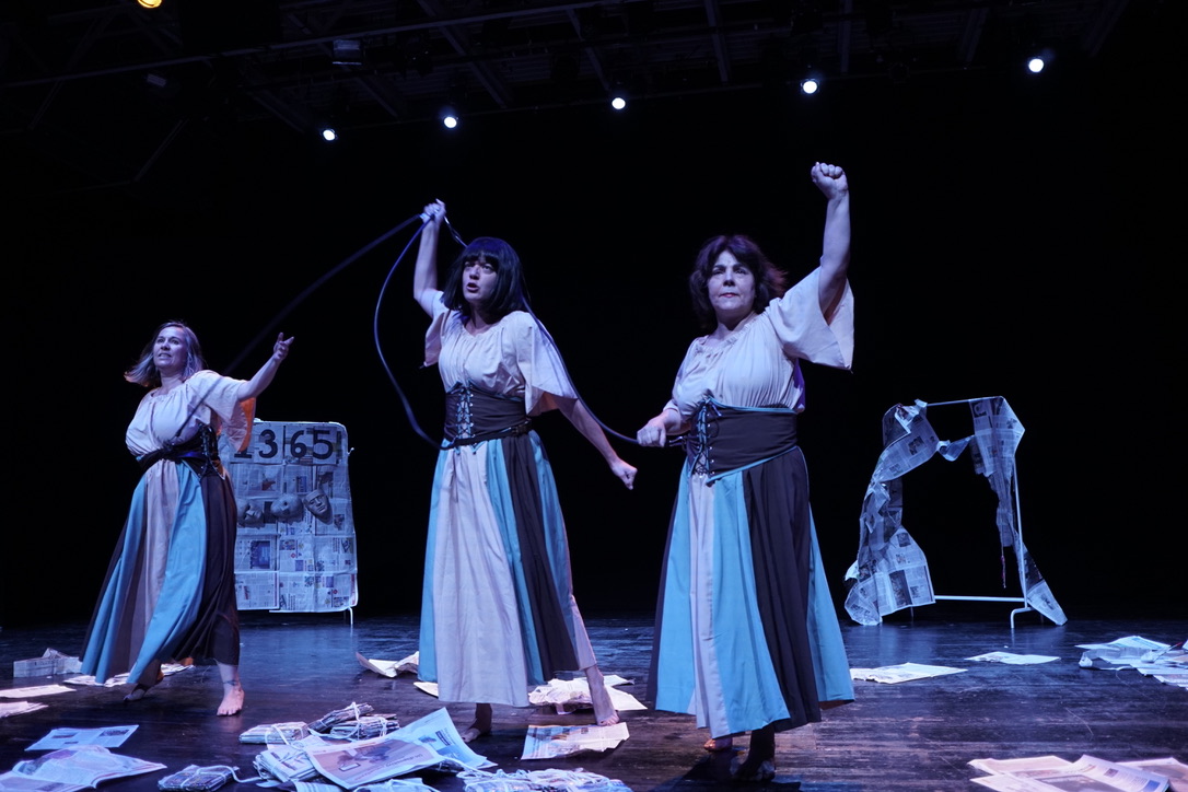 Escena teatral con tres intérpretes, vestuario y periódicos